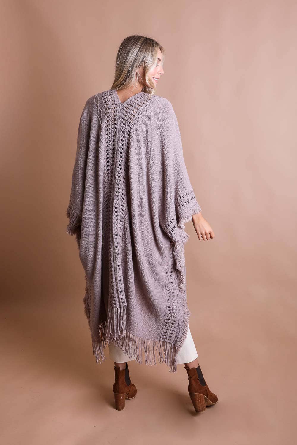 The back view of a blonde woman wearing a long gray fringed boho cardigan