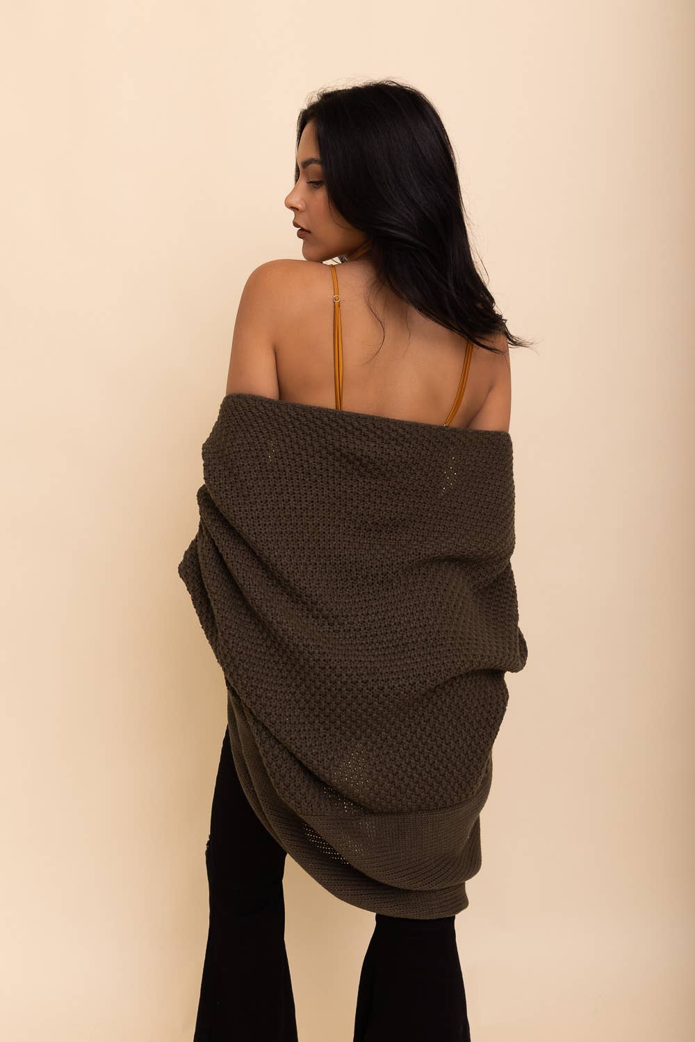 Back view of a young brunette woman wearing black jeans and an olive green bat wing cardigan.
