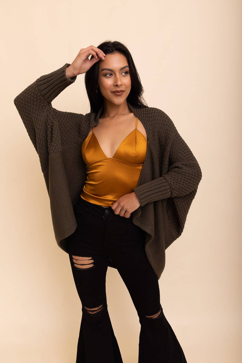 a young brunette woman wearing black jeans and an olive green batwing cardigan.
